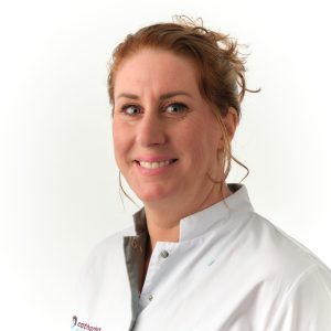 Vrouw met lichte huid en rossig haar in witte doktersjas lacht naar de camera tegen een witte achtergrond.